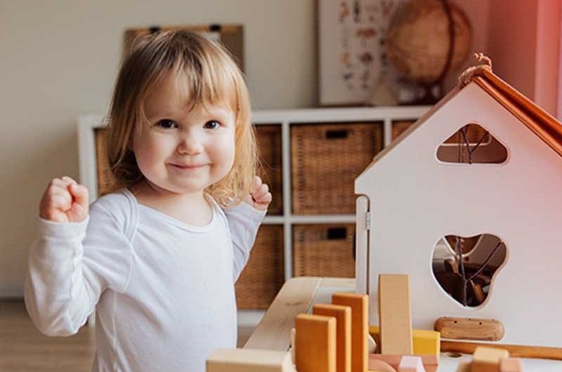 Kleines Mädchen freut sich über Spielhaus aus Holz