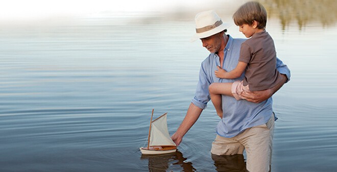 Vater spielt mit Sohn und einem kleinen Segelboot im Bodensee
