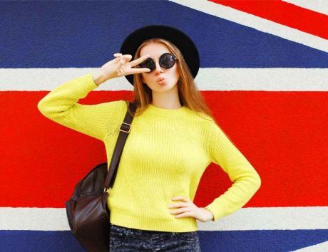 Junges Mädchen im gelben Pulli und Sonnenbrille posiert vor der englischen Landesfahne