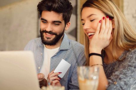 Frau und Mann schauen lachend auf Laptop-Bildschirm