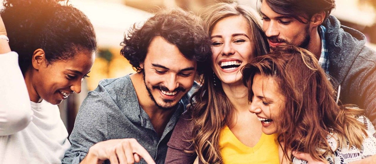 Mehrere junge Leute schauen glücklich lachend auf ein Smartphone