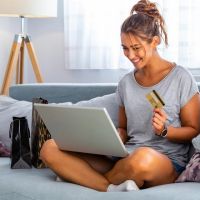 Frau sitzt auf Sofa und bezahlt beim Online-Shopping mit ihrer Mastercard Gold (Kreditkarte)